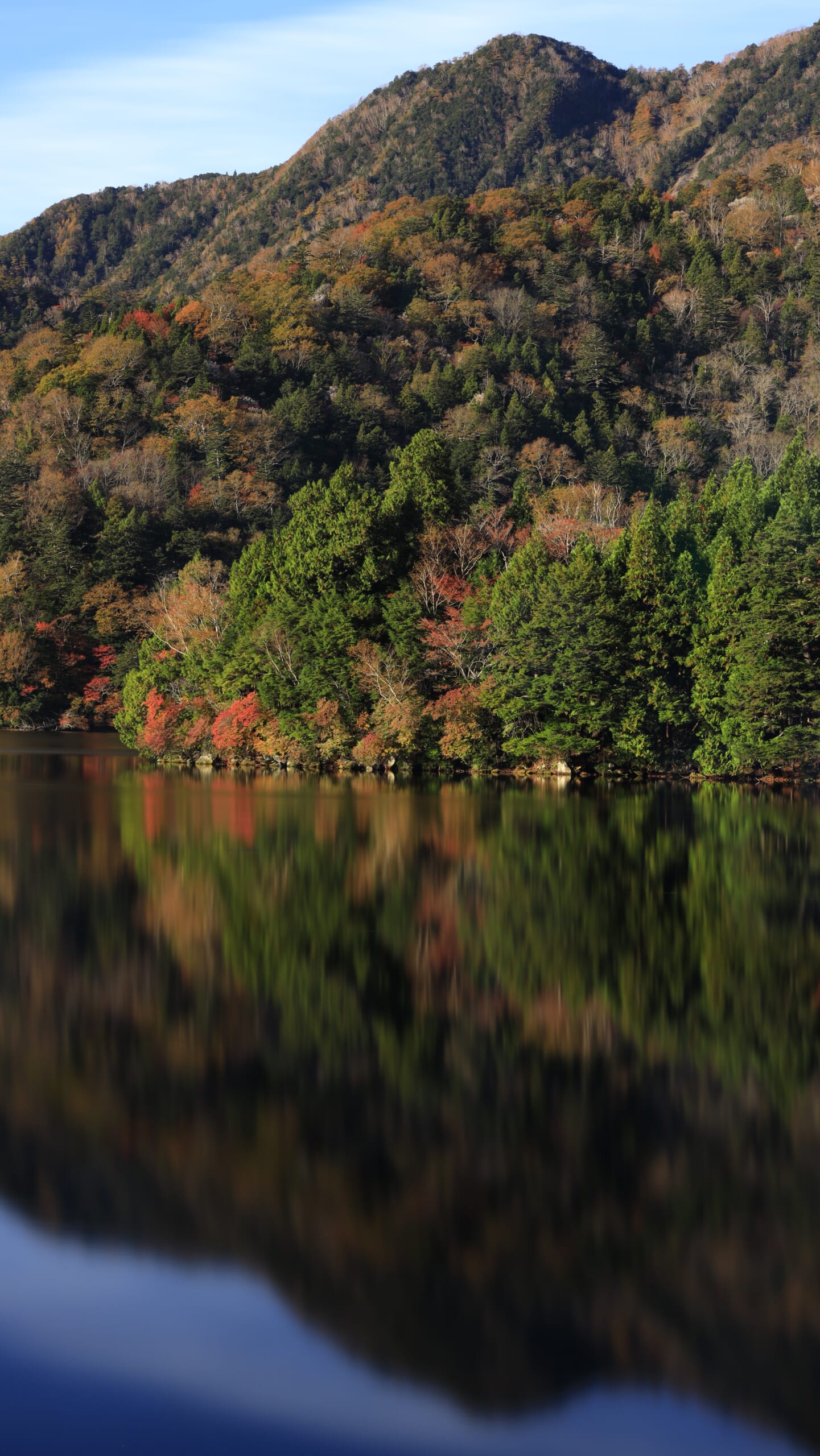 奥日光の湯ノ湖で、色づき始めた湖畔の紅葉が水面に映り込む、スローシャッターによる静かな秋のリフレクション